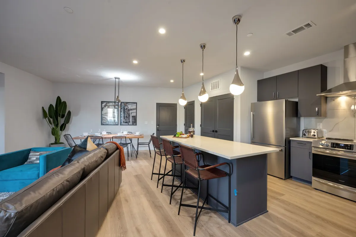 A modern open-concept kitchen and dining space featuring a welcoming kitchen island, a contemporary dining table, comfortable seating, and greenery for a vibrant touch. The design unites functionality with a sense of warmth and togetherness.