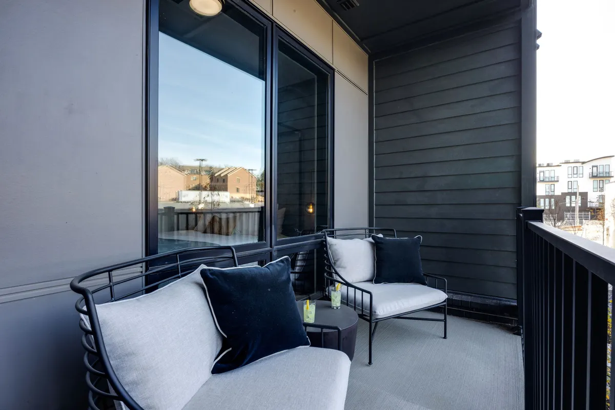 An exterior shot of a private balcony with comfortable seating and a small table, set against large windows. The scene is peaceful, perfect for morning coffee or evening drinks while enjoying city views.