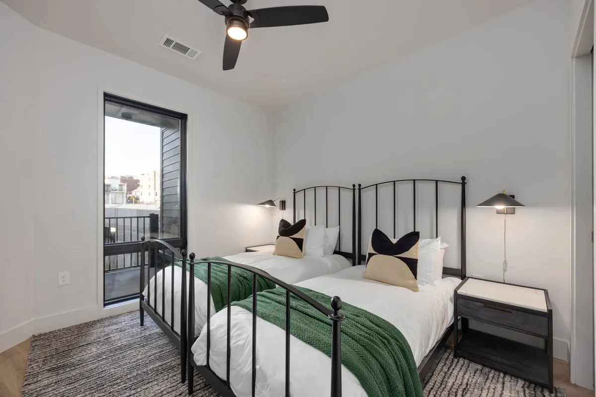 A cozy second bedroom with twin beds featuring black metal frames, a green throw blanket, and decorative pillows. The room feels inviting and practical—perfect for families or friends sharing a space. The overall atmosphere is relaxed and welcoming.