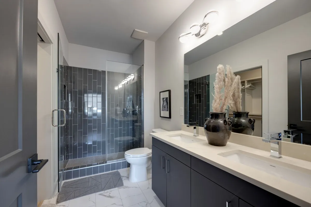A spa-inspired bathroom with a double vanity, a large walk-in shower, a decorative vase with pampas grass, and framed artwork. The space is bathed in soft light, creating a serene, luxurious environment for self-care and relaxation.