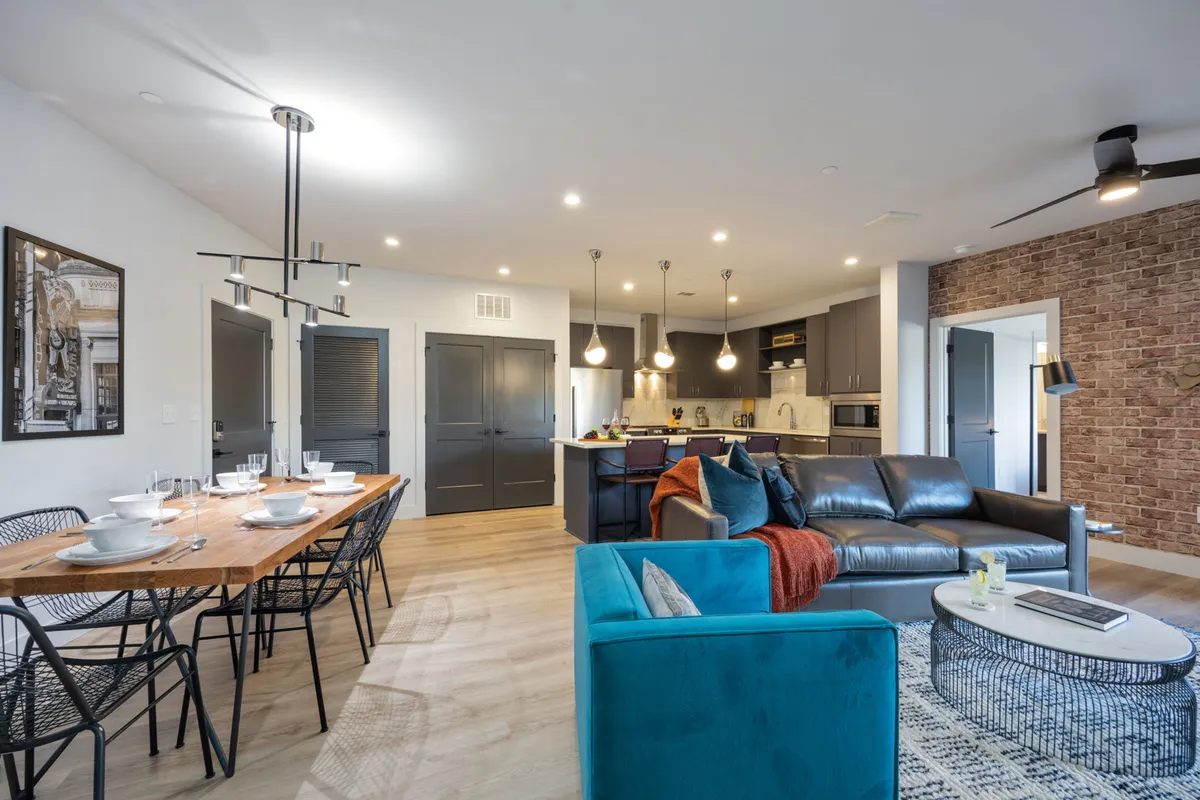 A welcoming view of the dining table set near a blue sofa and kitchen island, with contemporary design elements and warm, cozy lighting. The space feels inviting for both casual meals and festive celebrations.