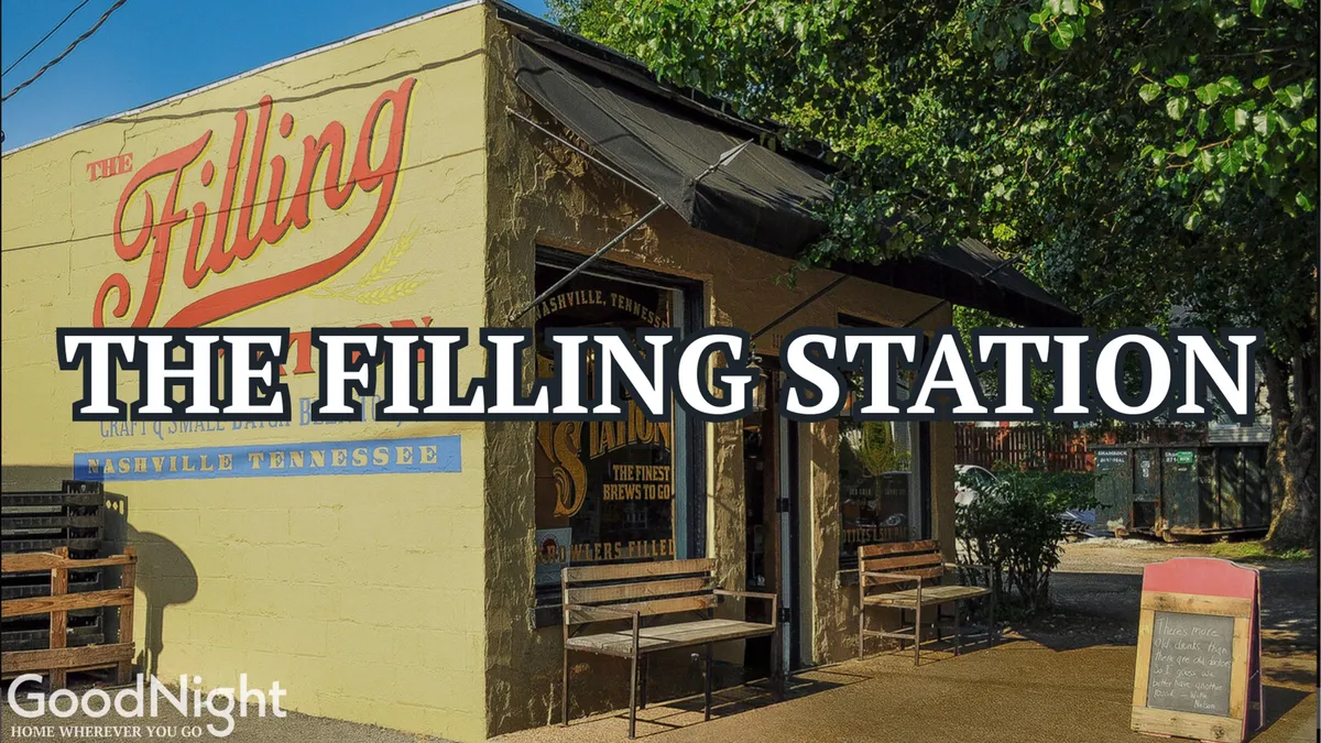 A casual outdoor dining area featuring The Filling Station sign, chalkboard menu, and people enjoying food and drinks in a relaxed social setting.