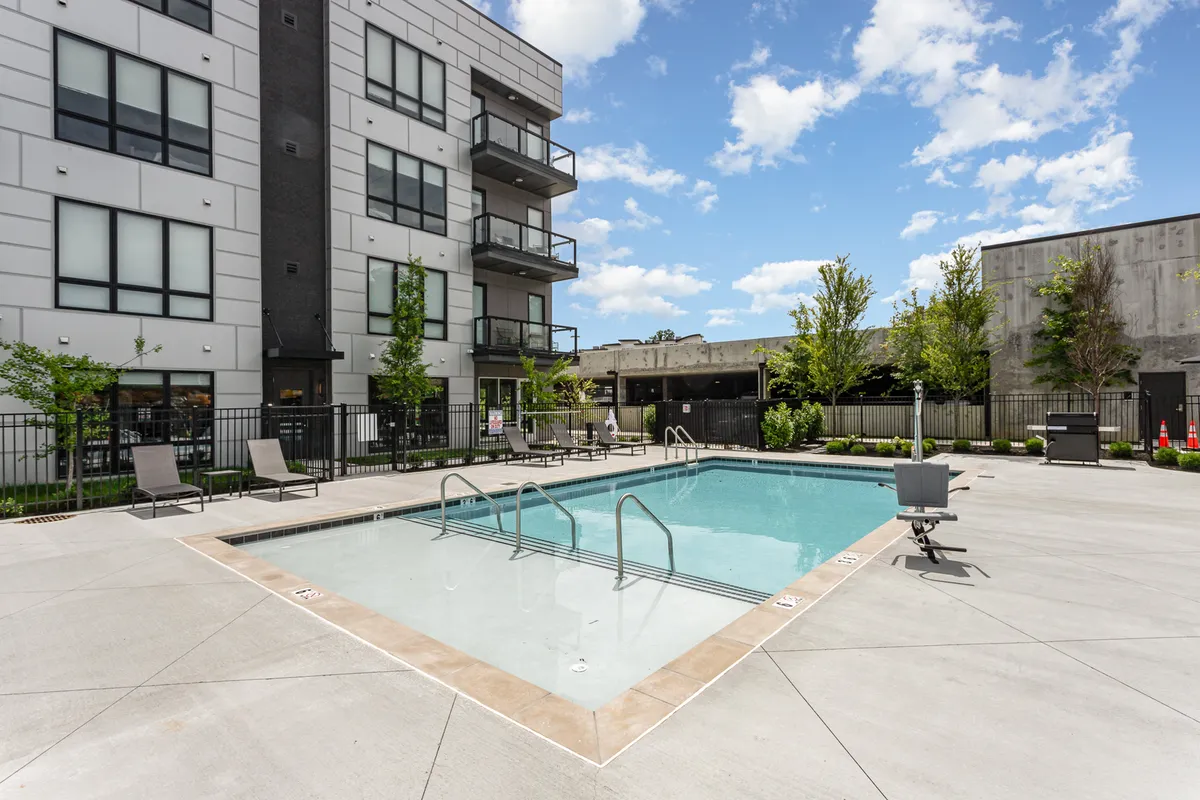 This photo highlights a sparkling outdoor swimming pool surrounded by greenery, with a modern apartment building in the background. The environment is relaxed and vibrant—ideal for families looking to unwind or socialize after a day out.